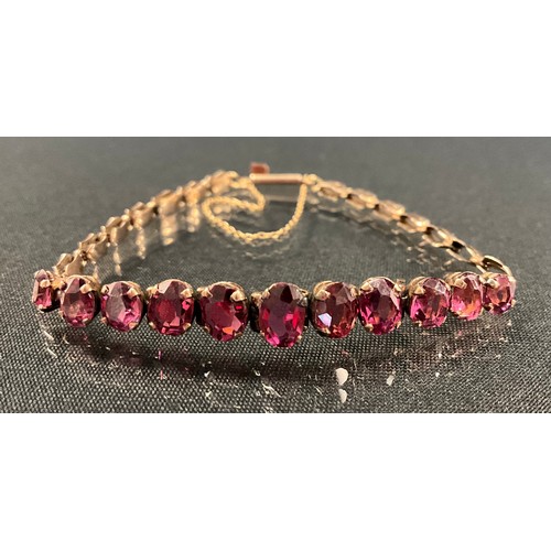 239 - A red  garnet bracelet, with eleven graduated mixed cut pinky red garnets, unmarked rose metal mount... 