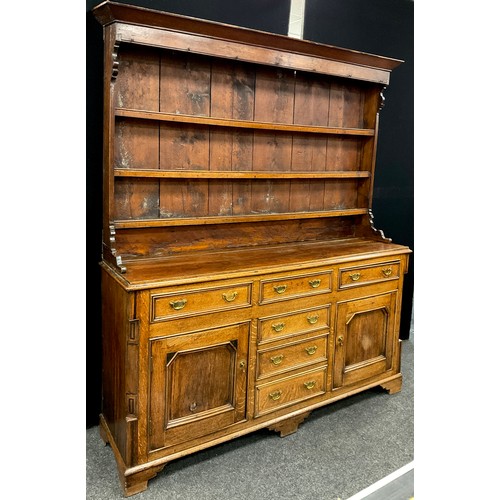 1215 - A George III revival oak dresser, the out-swept cornice above three tiers of plate-rack shelving, wi... 