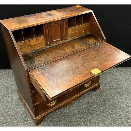 1122 - A George III oak bureau, fall front enclosing a fitted architectural interior, above four long gradu... 