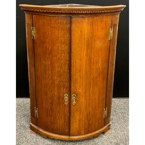 1121 - A George III oak bow-front corner cupboard, the Greek-key cornice above a pair of quarter-sawn oak d... 