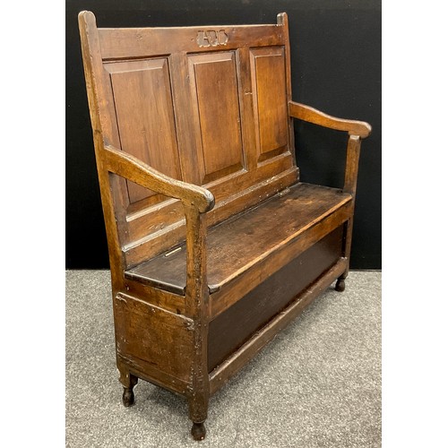 874 - An 18th century oak box settle, the tall back with three rectangular raised and fielded panels, carv... 