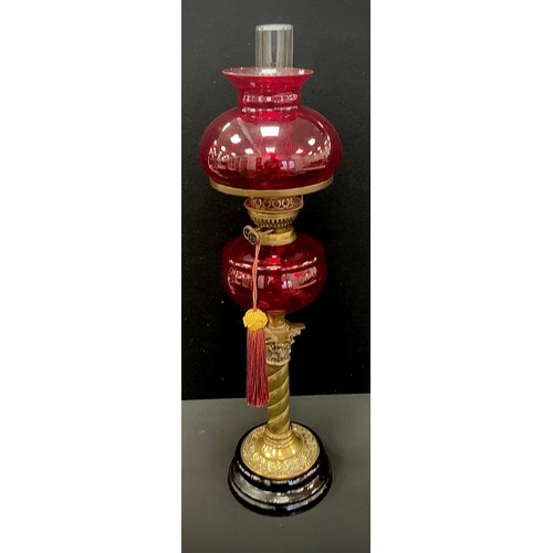 1027 - A Victorian style ruby glass and brass oil lamp, ruby reservoir and shade, spiralled column, black f... 