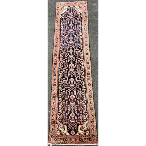 1085 - A large Persian Navahand runner carpet, hand-knotted with a central field of stylised flowers on a d... 