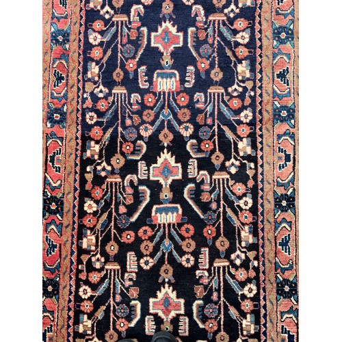 1085 - A large Persian Navahand runner carpet, hand-knotted with a central field of stylised flowers on a d... 