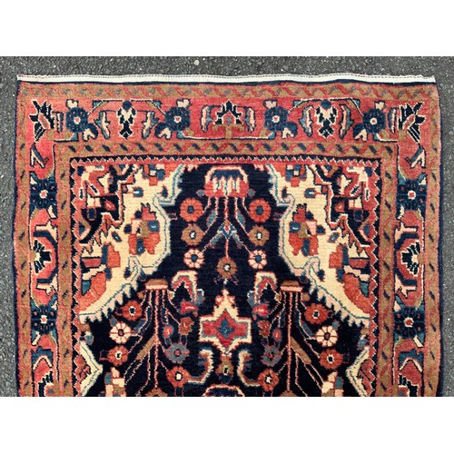 1085 - A large Persian Navahand runner carpet, hand-knotted with a central field of stylised flowers on a d... 