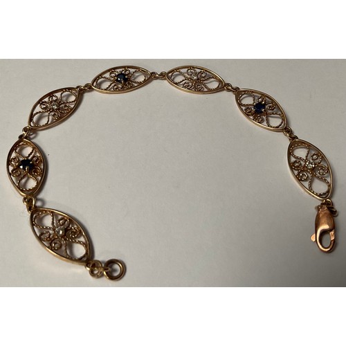 417 - An unmarked gold openwork filigree bracelet, the seven oval links set alternately with sapphire and ... 