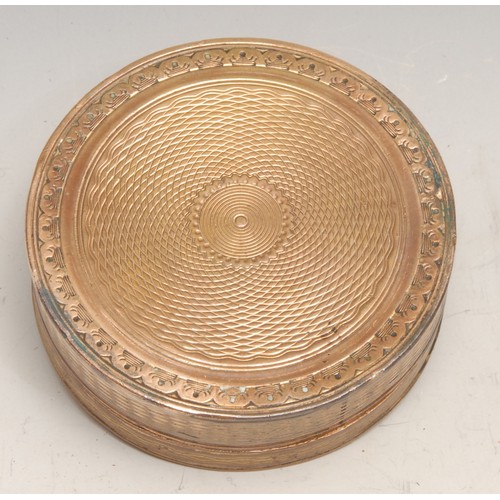 3099 - A late 18th century gilt copper circular snuff box, engine turned and chased with triumphal regalia,... 