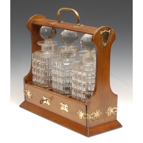 3105 - A late Victorian oak three-bottle tantalus, the fall-front base applied with brass cut-card work, 35... 
