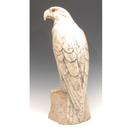 3023 - A carved alabaster model, of an eagle, perched on a rocky outcrop, glass eyes, 46cm high, 20th centu... 