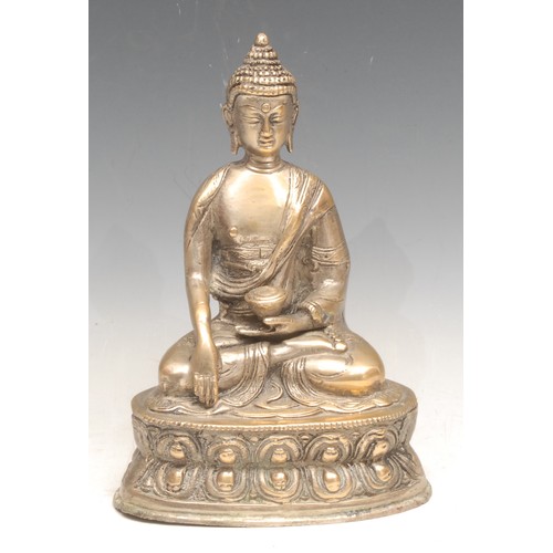 3333 - An Indian silver coloured metal figure of a seated Buddha, holding an ingot, seated on a lotus base,... 