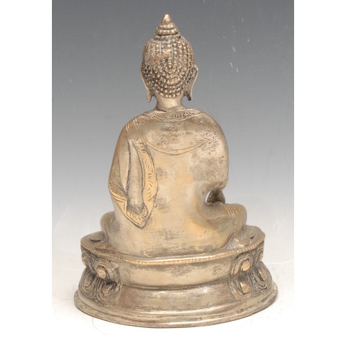 3333 - An Indian silver coloured metal figure of a seated Buddha, holding an ingot, seated on a lotus base,... 