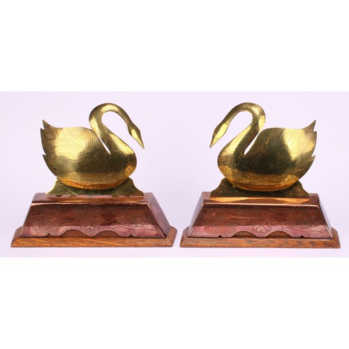 24 - A pair of Arts and Crafts brass, copper and oak mantle of hearth ornaments, as swans, beaten and fin... 