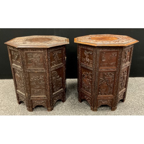 64 - A pair of Chinese hardwood octagonal folding occasional tables, each well carved with narrative subj... 