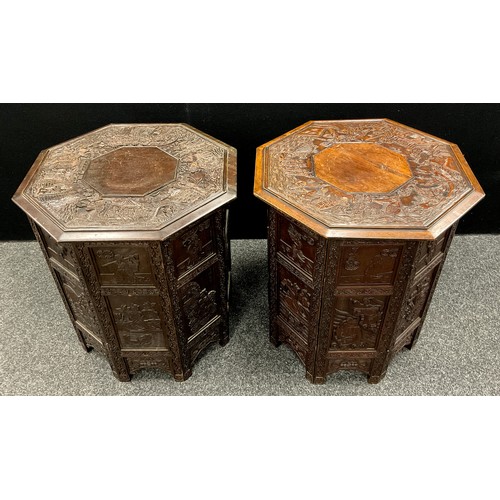 64 - A pair of Chinese hardwood octagonal folding occasional tables, each well carved with narrative subj... 