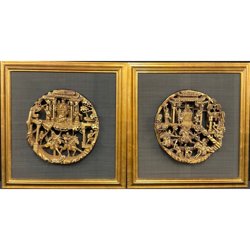 62 - A pair of Chinese giltwood circular panels, in bold relief with warriors on horseback beneath a temp... 