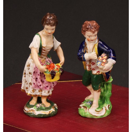 106 - A matched pair of Derby figures, Boy and Girl with Fruit and Flowers, he stands holding a basket of ... 