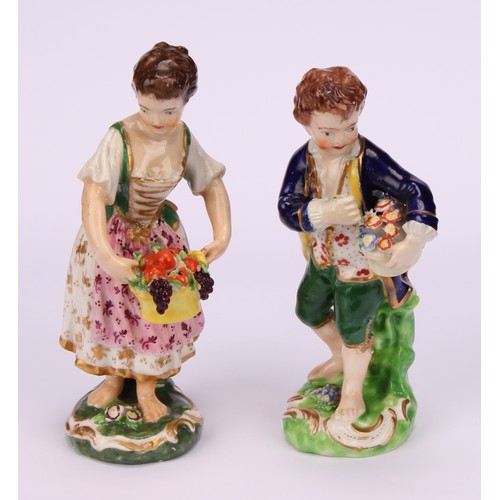 106 - A matched pair of Derby figures, Boy and Girl with Fruit and Flowers, he stands holding a basket of ... 