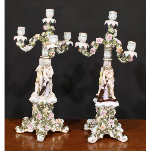 151 - A pair of Sitzendorf porcelain four-light figural candelabra, each modelled as putti holding oars an... 