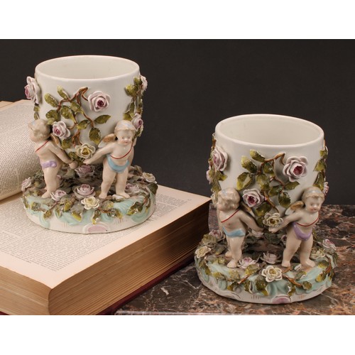 150 - A pair of Sitzendorf porcelain cache pots, each supported by four cherubs, the shaped circular base ... 