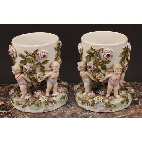 150 - A pair of Sitzendorf porcelain cache pots, each supported by four cherubs, the shaped circular base ... 