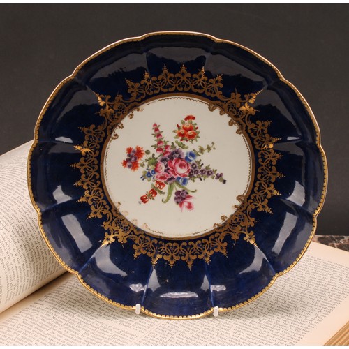 82 - A Worcester lobed dish, painted with a vignette of colourful flowers within scrolling gilt foliage, ... 