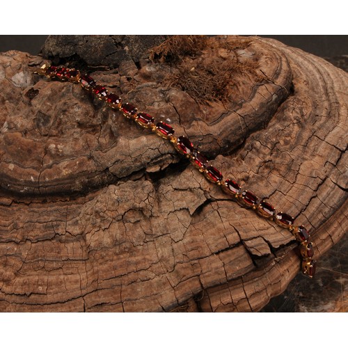 945 - A garnet bracelet, set with a continuous band of nineteen graduated oval cut stones, claw set, unmar... 