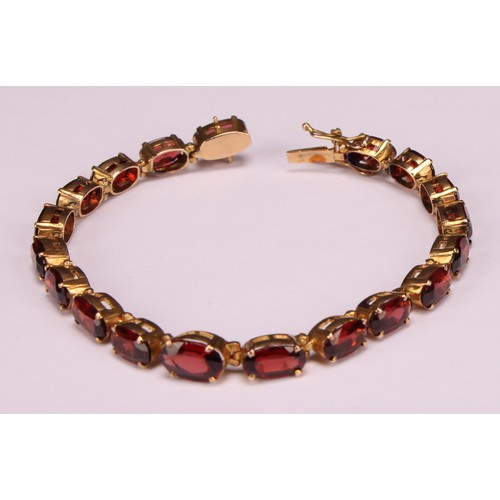 945 - A garnet bracelet, set with a continuous band of nineteen graduated oval cut stones, claw set, unmar... 