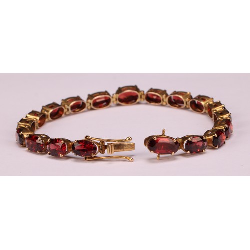 945 - A garnet bracelet, set with a continuous band of nineteen graduated oval cut stones, claw set, unmar... 