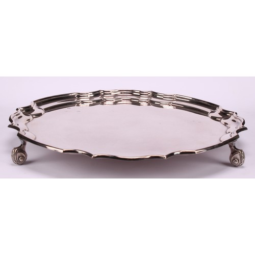 625 - A George II style silver shaped circular salver, plain field, piecrust border, foliate scroll feet, ... 