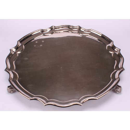 625 - A George II style silver shaped circular salver, plain field, piecrust border, foliate scroll feet, ... 