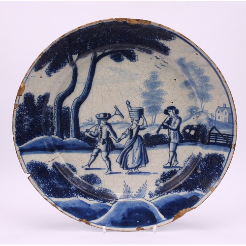 20 - An 18th century Delft circular dish, painted in tones of blue with gardeners and a musician, 29cm di... 