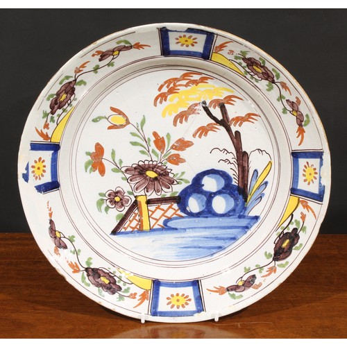 20A - An 18th century Dutch Delft charger, painted in polychrome, with flowers, tree and trellis, 34.5cm d... 