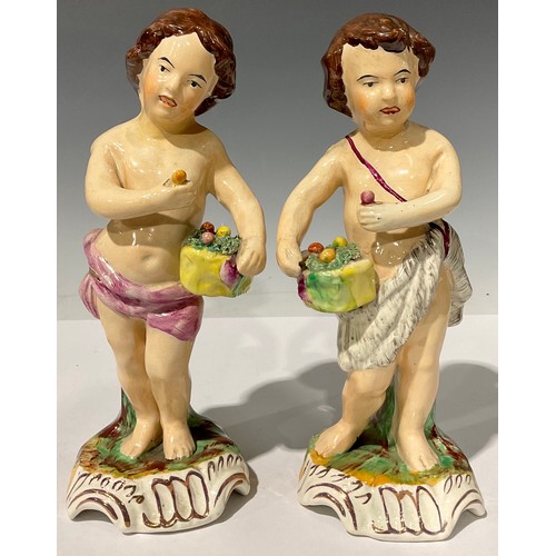 674 - A pair of 19th century Staffordshire figures, each as putti with baskets of fruit, in polychrome, sh... 