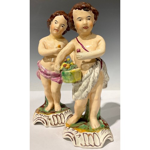 674 - A pair of 19th century Staffordshire figures, each as putti with baskets of fruit, in polychrome, sh... 