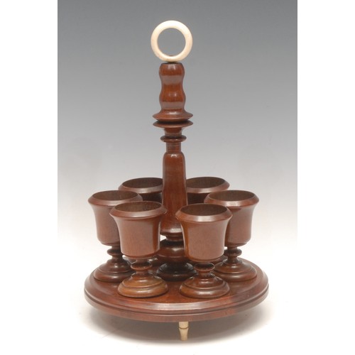 1032 - Treen - an Edwardian mahogany egg cup stand, bone carrying loop above turned column surrounded by si... 