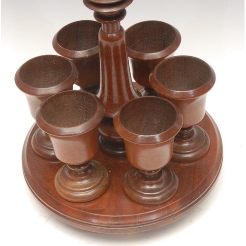 1032 - Treen - an Edwardian mahogany egg cup stand, bone carrying loop above turned column surrounded by si... 