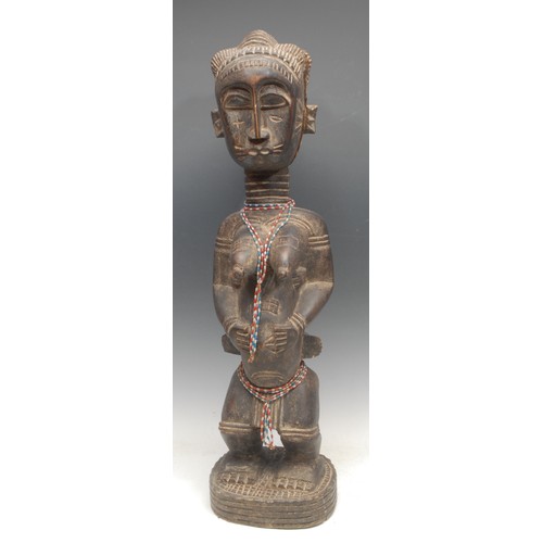 9 - Tribal Art - a Baule fertility figure, typically depicted kneeling, elaborate coiffure, 70cm high, I... 