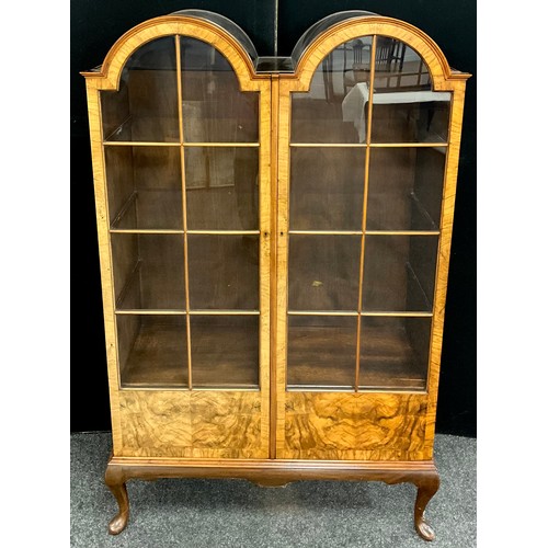 29 - An early to mid 20th century walnut double-arch top cabinet, glazed doors, three tiers of wooden she... 