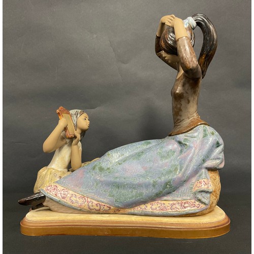 43 - A large Lladro figure group, Tying The Ribbon, 34cm high, shaped wooden plinth