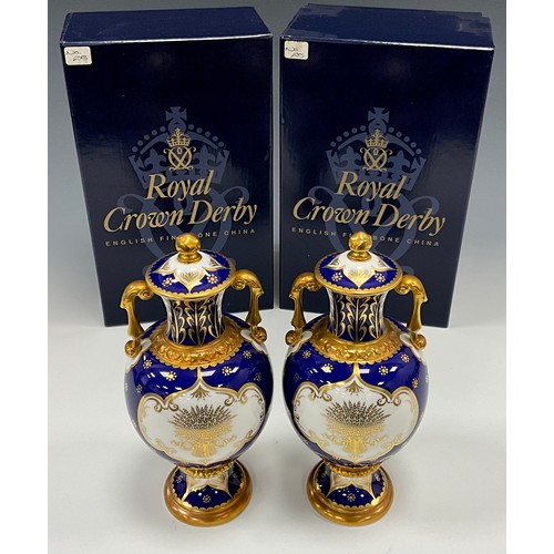 1337 - A pair of limited edition Royal Crown Derby vases and covers comprising a cobalt blue twin handled v... 