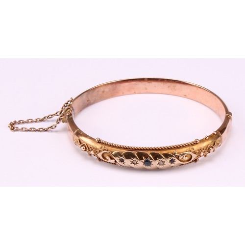 523 - A 19th century 9ct gold hinged bangle, set with diamond and sapphire chips, safety chain, 12.1g