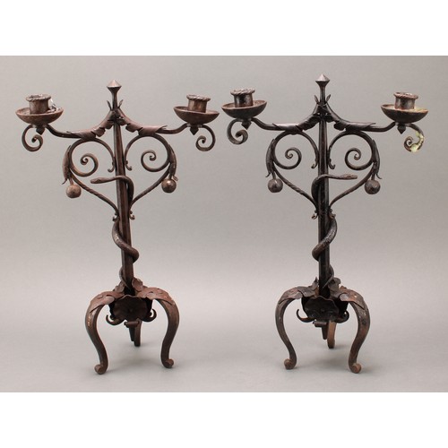 1849 - A pair of Arts and Crafts wrought iron two-light candelabra, the each pillar entwined with a serpent... 