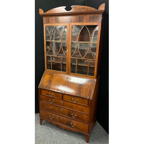 1911 - A Sheraton Revival mahogany bureau bookcase, shaped pediment above a pair of astral glazed doors enc... 