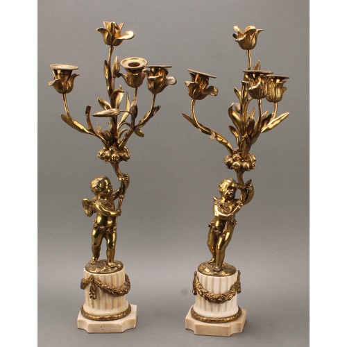 1845 - A pair of 19th century gilt metal candelabra, each cast as a scantily clad putto holding flowering b... 