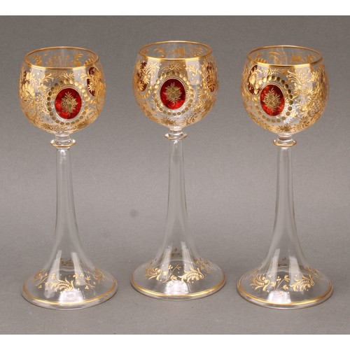 1372 - A set of three Bohemian etched and gilt harrach or wine glasses, the globular bowls with three oval ... 