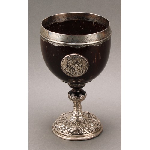 449 - An 18th century silver mounted pedestal coconut cup, the ovoid bowl applied with portrait roundels, ... 