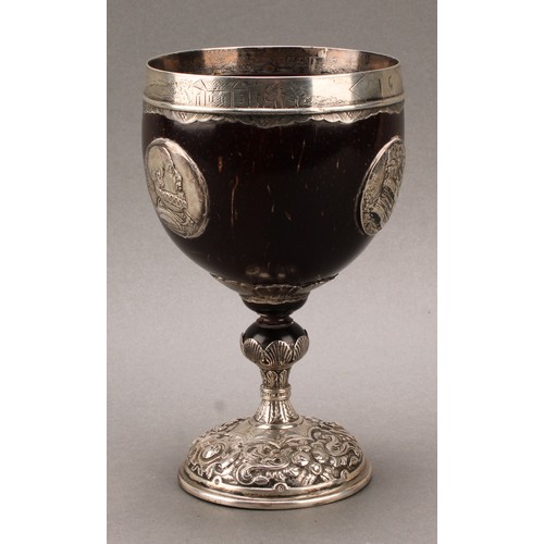 449 - An 18th century silver mounted pedestal coconut cup, the ovoid bowl applied with portrait roundels, ... 