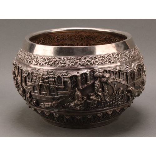 226 - A large Burmese silver bowl, repousse chased in bold relief with deities in a palatial setting, lotu... 