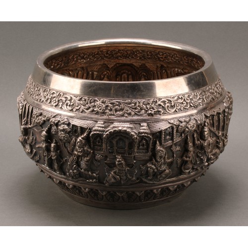 226 - A large Burmese silver bowl, repousse chased in bold relief with deities in a palatial setting, lotu... 