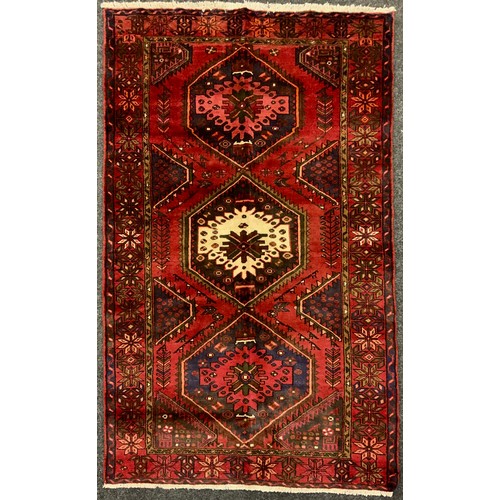 2068 - A Hamadan rug, knotted with a central row of three hexagonal shape medallions, in rich tones of red,... 